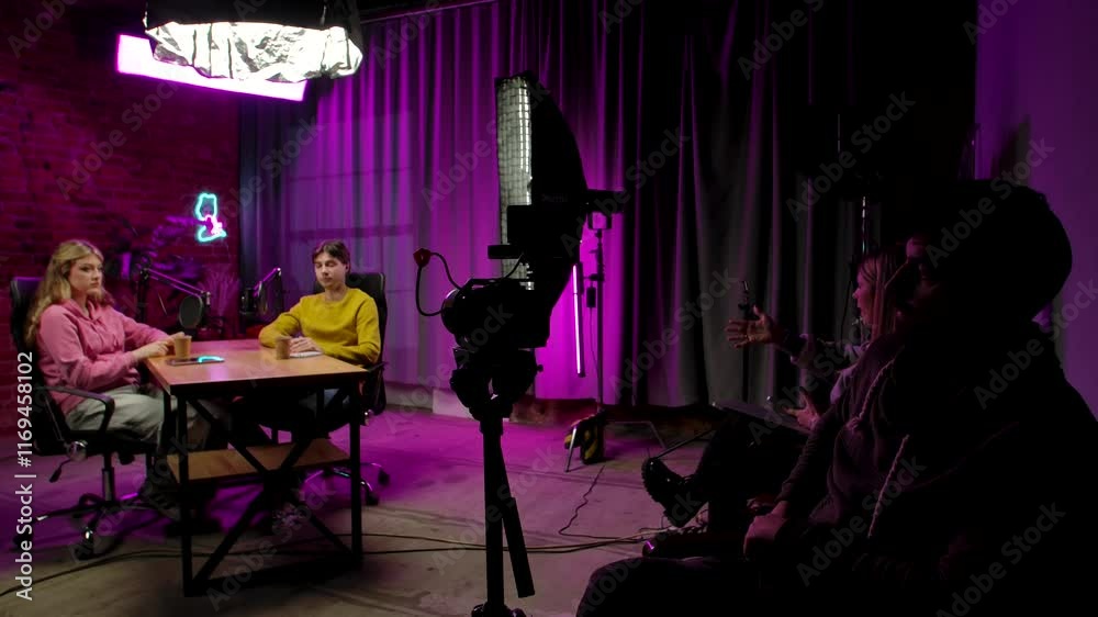 Backstage shot of interview in loft podcast studio, man host and woman guest finishing talk, ending recording and say goodbye, cameraman and producer control process at side.