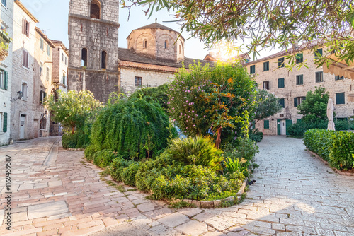 Picturesque medieval square in Kotor Montenegro with stone buildings lush greenery blooming flowers cobblestone streets and historic church creating a serene and charming travel destination atmosphere