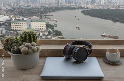 Obraz na płótnie Relaxation area or Working space in Condominium balcony overlooking city view. Laptop, Ear headphones, Tea cup and Cactus pot on Wooden table, use it as your Wallpaper, Poster and Space for text. w salonie