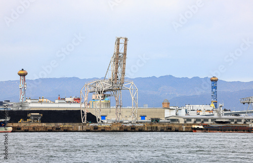 Large crane works on large coal stockpile and container at Industrial port. Cargo transportation and activity at modern shipping container terminal.