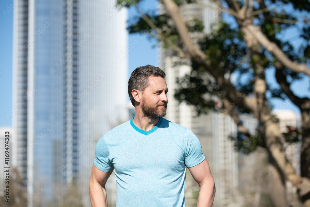 Fototapeta premium Outdoor male portrait. Man in blue t-shirt posing near American city. Happy business man posing outside. Businessman. Business man in t-shirt. American owner, casual businessman.