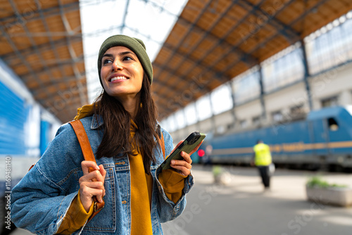 A modern traveller, a young woman with a backpack, using her smartphone to plan her next steps at the train station