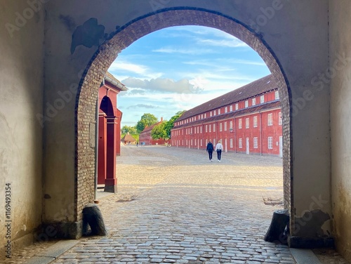 View Through a Brick Archway Framing Red Barracks, Cobblestone Path, and Two People Walking at Kastellet Fortress, Copenhagen, Denmark