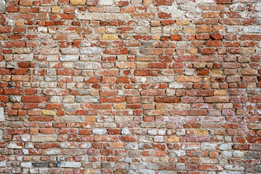 Brick wall with pieces of plaster. Wall of an old building in need of renovation. Aged wall texture of brick building close up. Grunge background with red and white blocks and layers of cement stucco