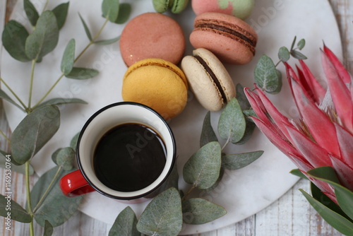 Cup of coffee, macarons in different colors and tastes and fresh protea flower and eucalyptus photo