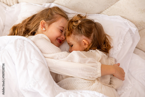 Cheerful little girls, two sisters in white dresses in bed. Children lying in bed and hugging each other. Good morning. textiles for the nursery. Have a nice day. High quality photo photo