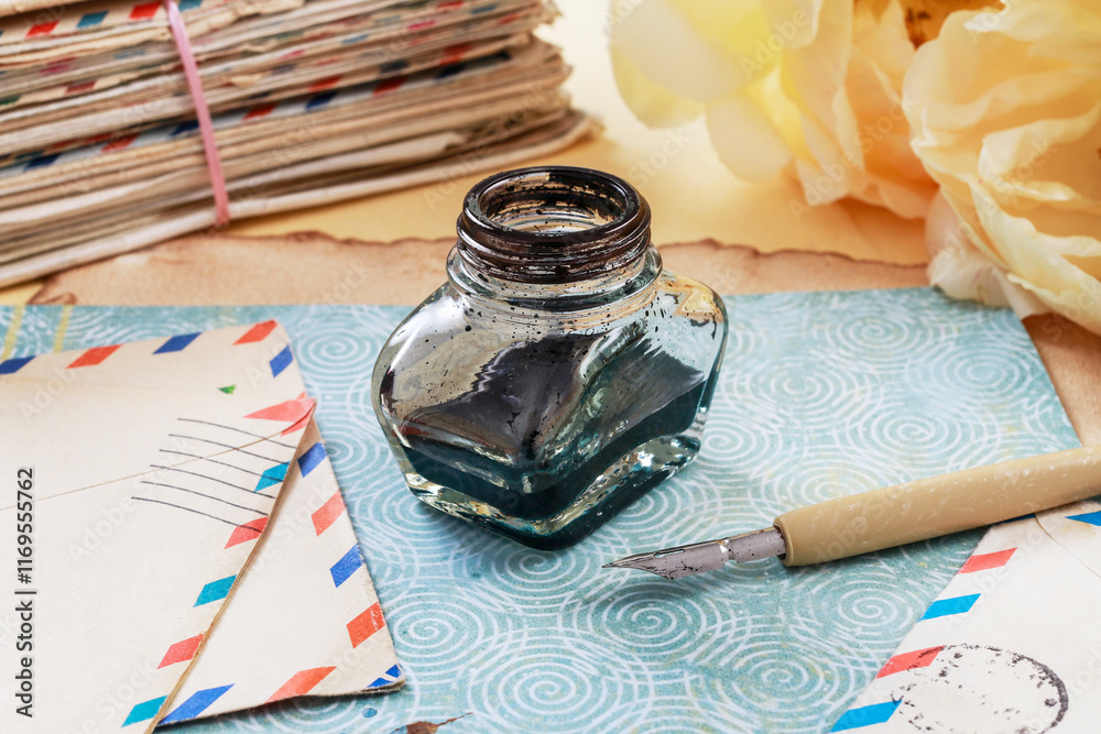 Inkwell, pen, vintage letters and peony flowers in the background.