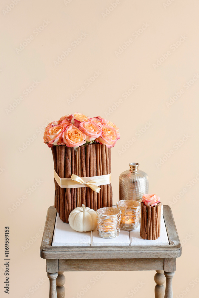 Floral arrangement with roses and cinnamon sticks stands on the table, small golden candle holders are by it's side.