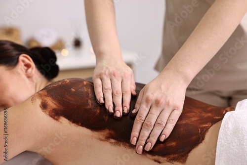 Woman undergoing chocolate body wrap treatment in spa salon, closeup photo