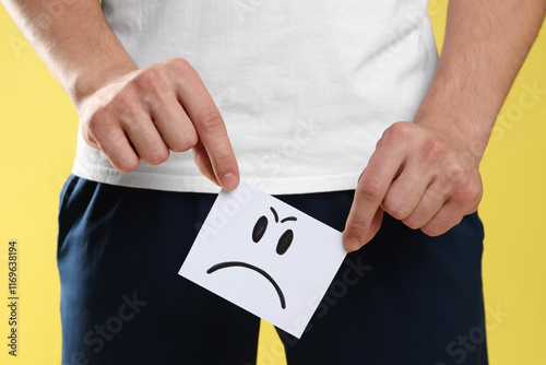 STD (sexually transmitted diseases). Man holding sticky note with drawn angry face on yellow background, closeup photo
