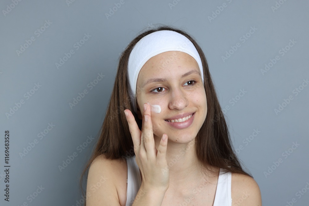 Teenage girl with acne problem applying cream on grey background Teenage girl with acne problem applying cream on grey background