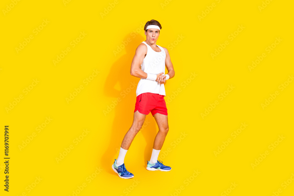 Energetic young athlete in red shorts performing warm-up exercise against a vibrant yellow background Energetic young athlete in red shorts performing warm-up exercise against a vibrant yellow background