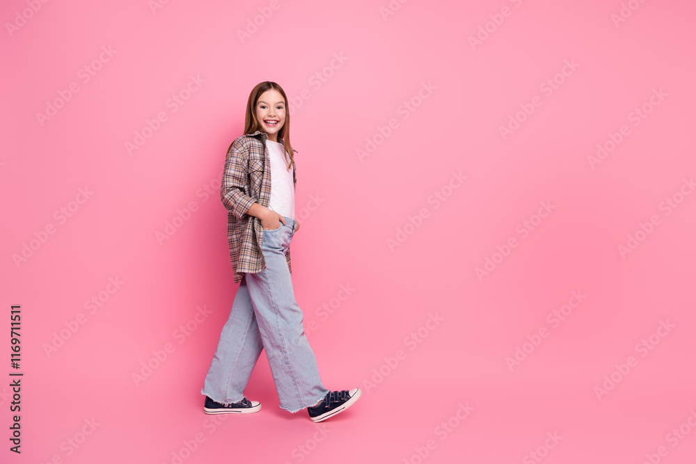 Stylish young girl in trendy outfit walking confidently on pink background, smiling charmingly Stylish young girl in trendy outfit walking confidently on pink background, smiling charmingly