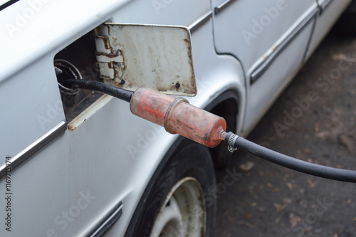 siphoning fuel from an old white car into a transparent plastic bottle black hose fuel tank container rural area emergency fuel solutions DIY fuel-saving tips off-grid living preparedness alternative 