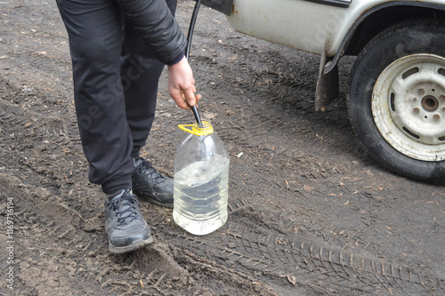 Foto siphoning fuel from an old white car into a transparent plastic bottle black hos
