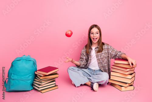 Smiling girl sitting surrounded by school books with a backpack against a pink background photo