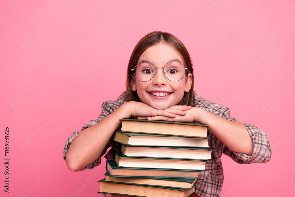 Smiling young girl with glasses and stacked books against a pink background embodying education and childhood joy Smiling young girl with glasses and stacked books against a pink background embodying education and childhood joy