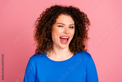 Cheerful young woman in casual blue sweatshirt winking playfully against a vibrant pink background