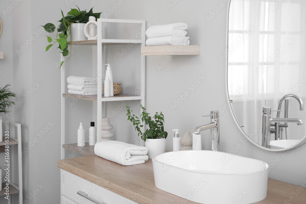 Fototapeta premium Folded clean towels with houseplants and cosmetic products on table in bathroom