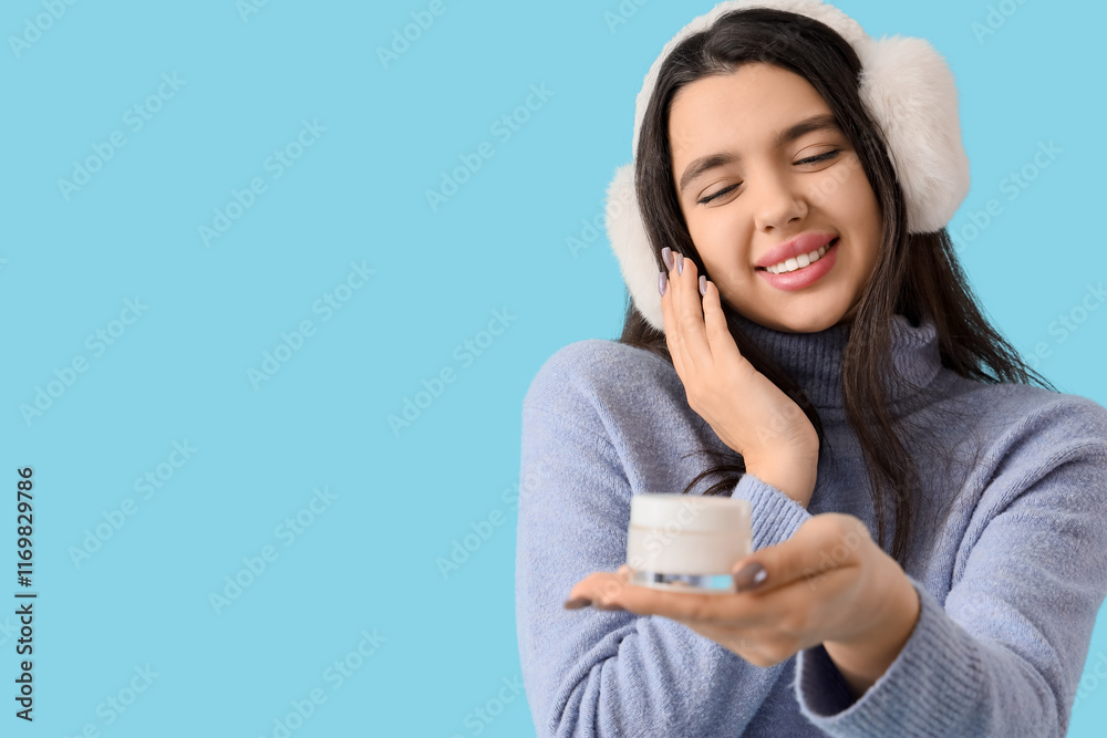 Young woman in winter clothes with jar of cream on blue background, closeup Young woman in winter clothes with jar of cream on blue background, closeup