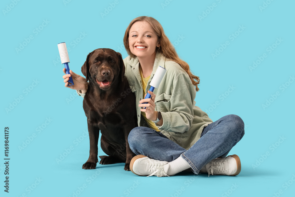Young woman with lint rollers and Labrador dog sitting on blue background Young woman with lint rollers and Labrador dog sitting on blue background