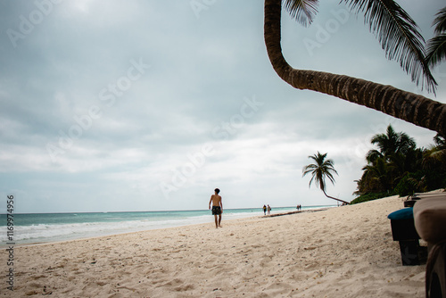 Young male walking on the beach from Tulum, Mexico, with a Palm Tree in the background