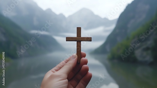 Hand holding a wooden cross by the riverbank. photo