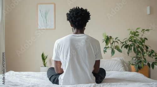 Man sitting on bed with back turned appearing contemplative and distressed after relationship issues in a cozy indoor environment photo