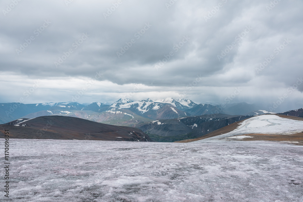 Dramatic panoramic view from big glacier to wide alpine valley and large snow-capped mountain range in rainy low clouds. Awesome vast landscape with high snowy mountains in rain under gray cloudy sky. Dramatic panoramic view from big glacier to wide alpine valley and large snow-capped mountain range in rainy low clouds. Awesome vast landscape with high snowy mountains in rain under gray cloudy sky.