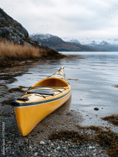 Yellow kayak is sitting in the water near a rocky shore. The scene is calm and peaceful, with the water reflecting the sky and the mountains in the background
