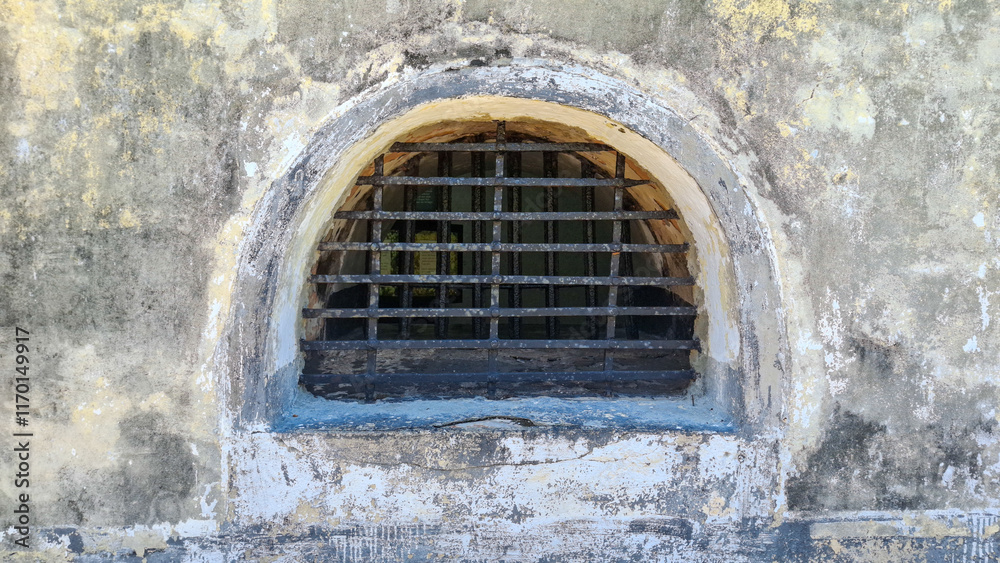 A barred arched window in a weathered stone wall evokes a sense of confinement, history, and the passage of time A barred arched window in a weathered stone wall evokes a sense of confinement, history, and the passage of time