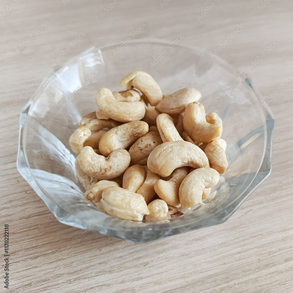 Glass transparent plate with cashews on a wooden table. Fatty amino acids in nuts. Fruits of the evergreen tropical tree Anacardium occidentale. Glass transparent plate with cashews on a wooden table. Fatty amino acids in nuts. Fruits of the evergreen tropical tree Anacardium occidentale.