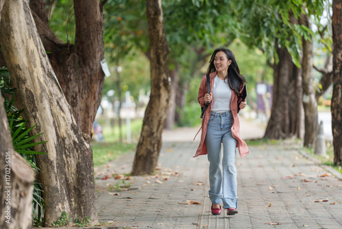 Happy confident young asian female university student walking on campus sidewalk with backpack and books, enjoying her education and smiling