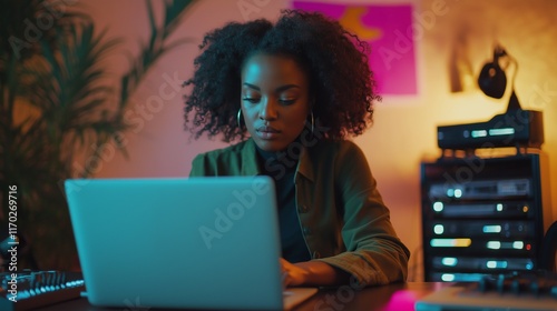 Focused Black woman working on laptop in creative workspace.