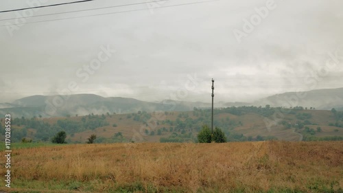 Panning shot of a rural area with hills, trees, mist and electric poles photo