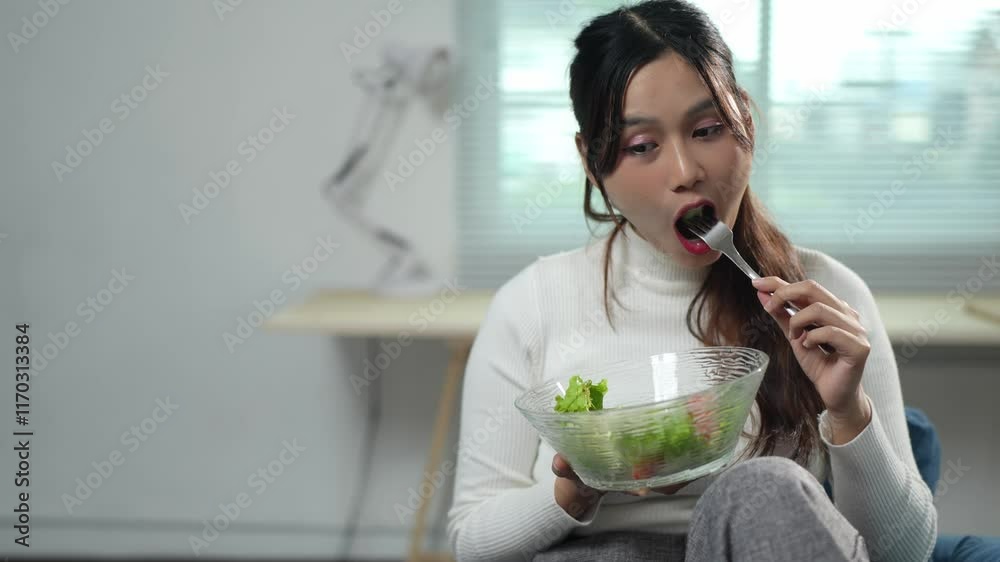 Attractive Asian woman Confidently holding a bowl of vegetable salad healthy food Controlling weight while working in your home office health care concept Food that is beneficial to the body. Attractive Asian woman Confidently holding a bowl of vegetable salad healthy food Controlling weight while working in your home office health care concept Food that is beneficial to the body.