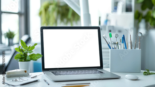 A mockup of a stylish fashionable laptop in the dentist's office. An open laptop sits on a desk with a mint pot and dental instruments. Dentist's Day. Caries treatment and prosthetics