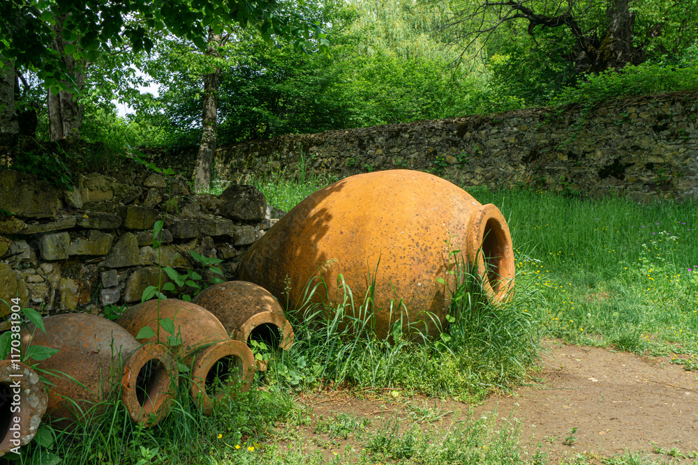Several Kvevri Qvevri Churi of different sizes on the grass near a stone wall. Earthenware clay vessel used for the fermentation, storage and ageing of traditional Georgian wine. Several Kvevri Qvevri Churi of different sizes on the grass near a stone wall. Earthenware clay vessel used for the fermentation, storage and ageing of traditional Georgian wine.