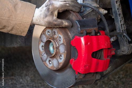 Person is working on a car's brake system, specifically the brake caliper. The caliper is red and has a black handle. The person is wearing gloves while working on the car