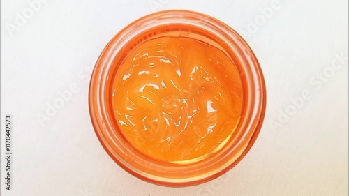 Vitamin C cream in a glass container isolated rotating on white background. lightweight gel like yellow-orange vitamin C cream. close up, top view