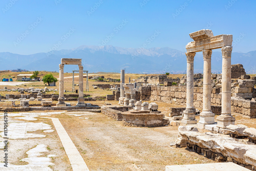 Fototapeta premium Ancient temple courtyard in Laodicea featuring marble columns, stone ruins, and a scenic mountain backdrop under a blue sky. Denizli, Turkey (Turliye)