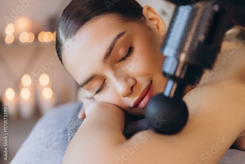 Masseuse performing massage therapy on relaxed client with percussion massager in spa