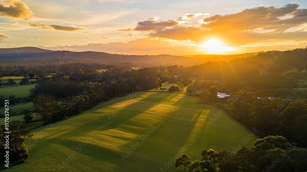 Obraz premium Aerial view of a stunning sunset over a rural landscape with golden hour light illuminating the green fields and forests.