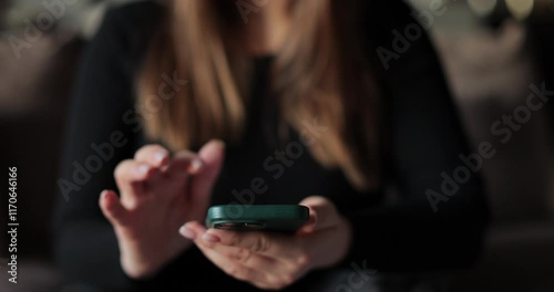 Close-up young woman using smartphone in living room at home. Girl using texting mobile phone or chat. Chatting on social networks online.