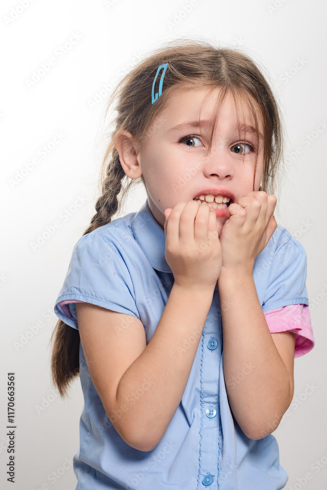 A young girl with braids, wearing a light blue shirt, displays a nervous expression, biting her nails. The image conveys anxiety or apprehension. A young girl with braids, wearing a light blue shirt, displays a nervous expression, biting her nails. The image conveys anxiety or apprehension.