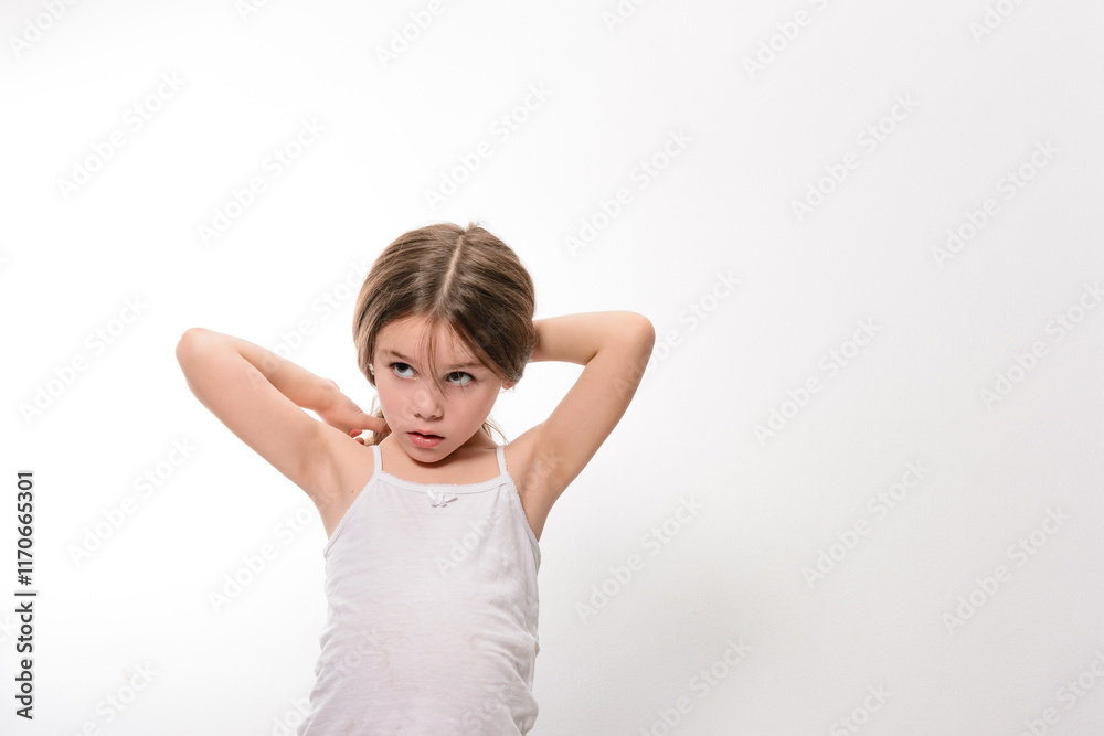 A young girl with light brown hair, wearing a white tank top, is seen thoughtfully adjusting her hair. The image is set against a simple white backdrop. A young girl with light brown hair, wearing a white tank top, is seen thoughtfully adjusting her hair. The image is set against a simple white backdrop.