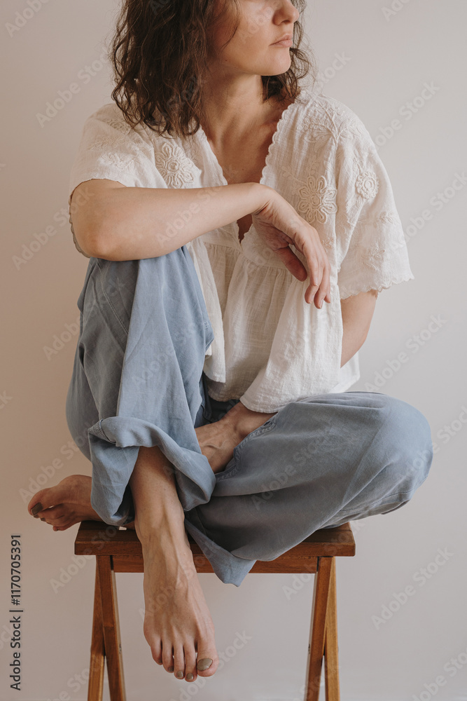 Φωτογραφία Woman Wearing Casual White Blouse and Jeans Sitting Cross-Legged on Wooden Stool