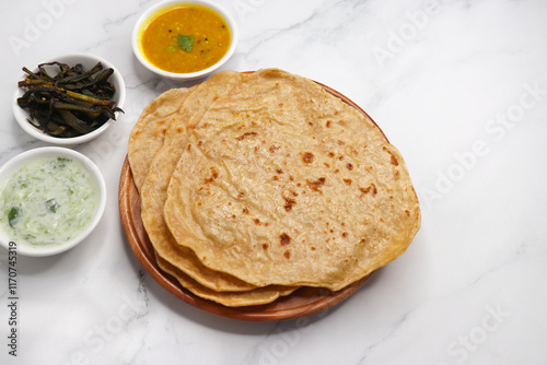 Roti and Sabzi. Indian vegetarian Thali includes bhindi fry, yellow daal tadka, cucumber raita, and chapati or tel paratha. Indian food is served in a plate or thali. Copy Space. healthy Veg Thali.  photo