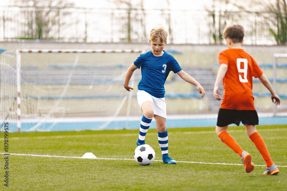 Obraz premium Young Soccer Players Running After the Ball. Kids in Soccer Red and Blue Uniforms. Soccer Stadium in the Background. Football Soccer Players Running with Ball. Footballers Kicking Football Match.