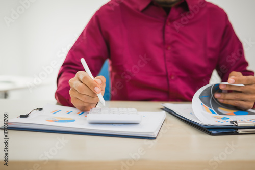A focused man works diligently in his office, reviewing numerous accounting documents on his desk. His goal is to ensure accuracy and precision, avoiding errors in critical financial data.